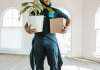 A person carrying a plant and box in an empty home.