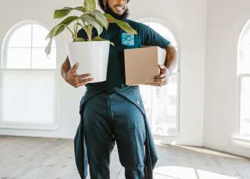 A person carrying a plant and box in an empty home.