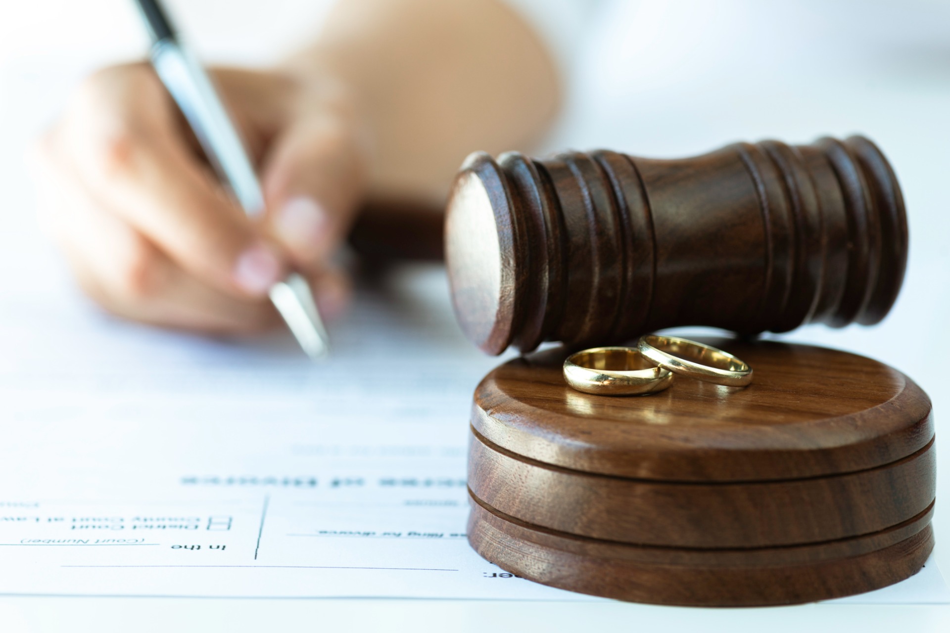 A person filling out paper work next to a gavel.