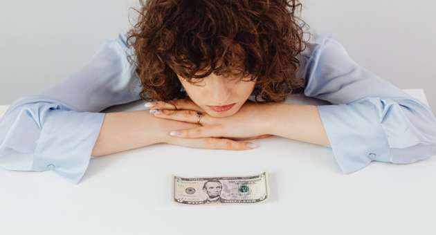 A woman looking at a five dollar bill.