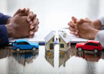 Two people sitting across from each other. They each sit with a miniature car and half of the same house.