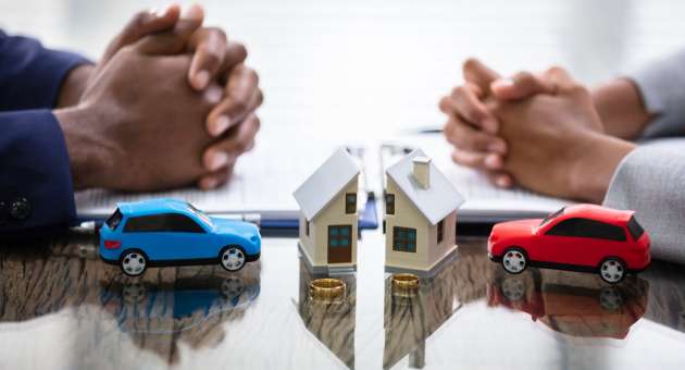 Two people sitting across from each other. They each sit with a miniature car and half of the same house.