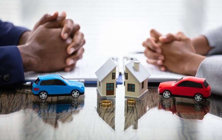 Two people sitting across from each other. They each sit with a miniature car and half of the same house.