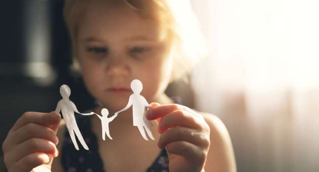 A little girl looking at a paper family in her hands.