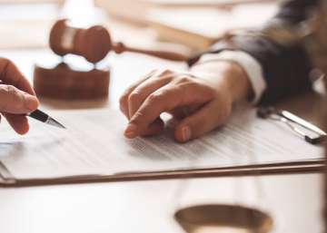 One person is about to sign documents. The other person points at something on the document.