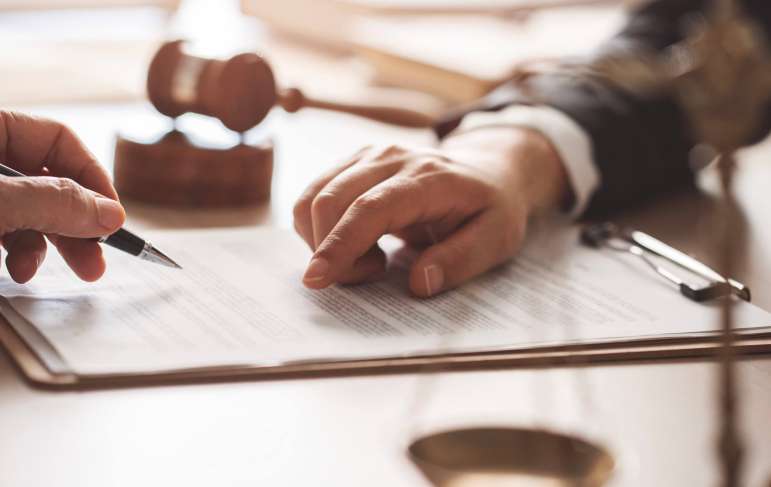 One person is about to sign documents. The other person points at something on the document.